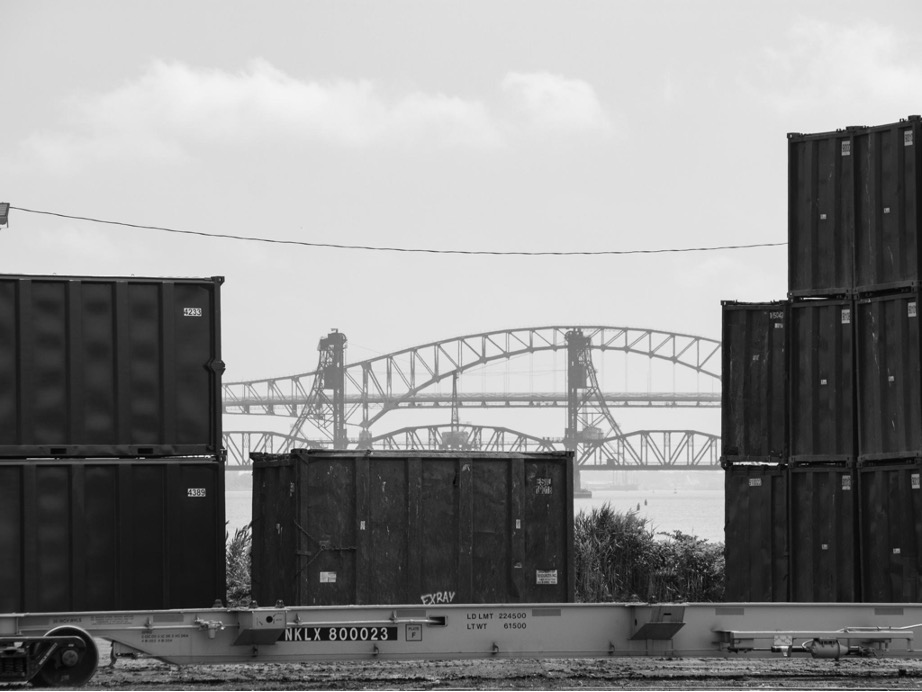 Some Interstate Waste Services trash containers frame the bridges over Newark Bay from the company's South Kearny terminal. Roads like the Jersey Turnpike, which runs over the taller of the two spans, were instrumental in facilitating industrial decentralization in New York. 07/2021
