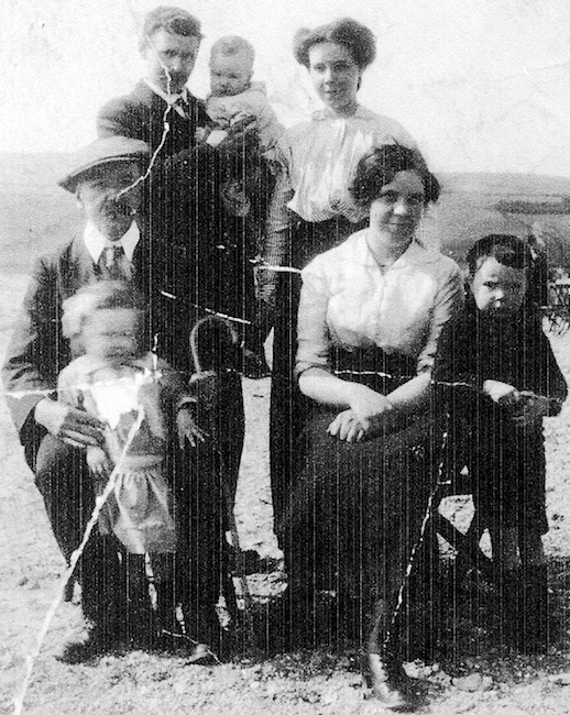 Black & white photograph of the family of Eachann Dòmhnallach, also known as Hector MacDonald, Mull View, Balemartine, taken off-island around 1914. Hector was a leader of the Tiree Land League during the `Crofters` War` of the 1880s. Sitting: Hector MacDonald with his grandaughter Catherine MacDonald, Margaret Clarke MacDonald (wife of John) with young Hector MacDonald; standing: Hector`s son John MacDonald and his son Archibald, and his sister Annie MacDonald. An Iodhlann.